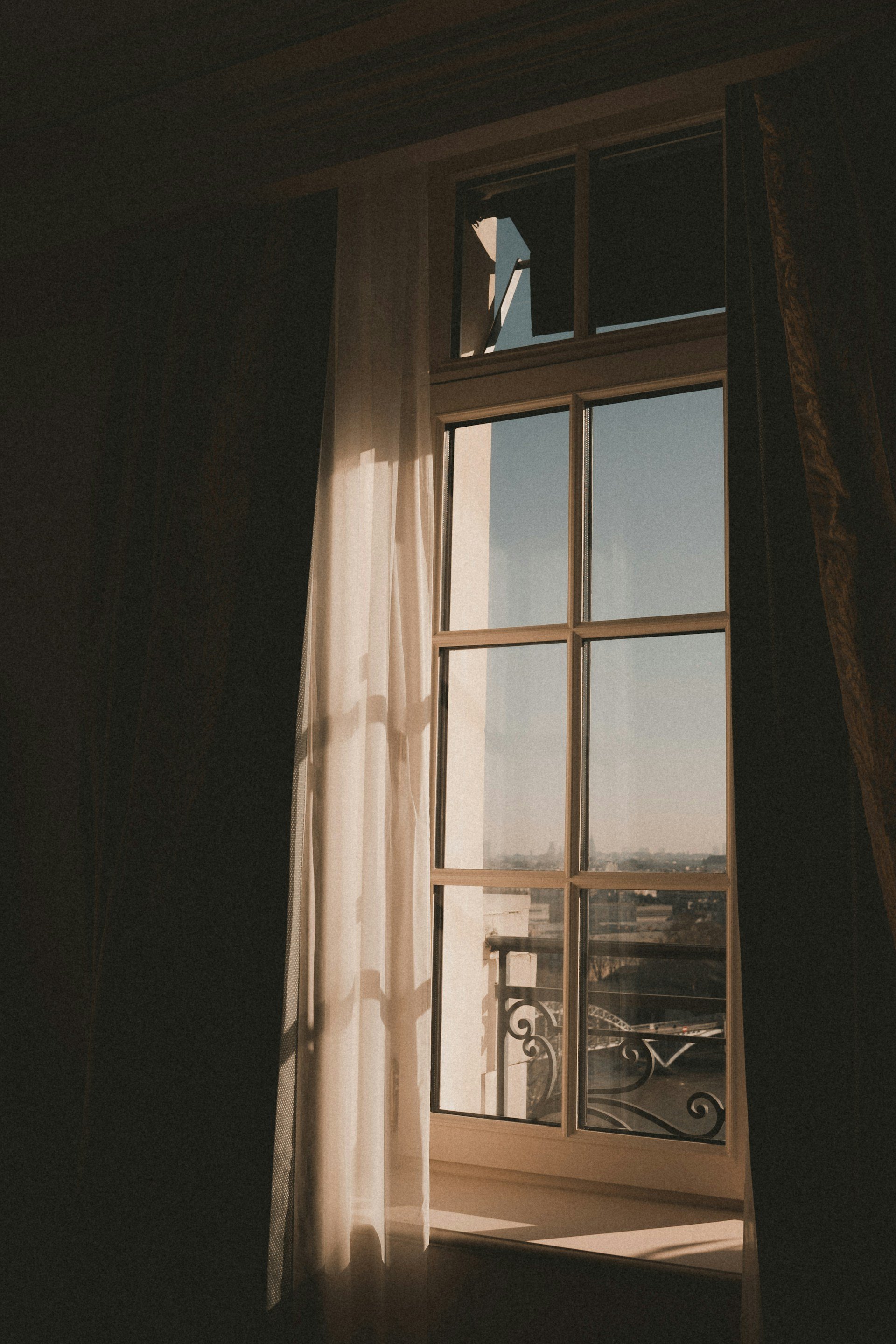 Wedding Website Design, Digital Wedding Stationery, Web Design and Branding for Wedding Professionals | Avelã White. Sunlight streaming through a window with sheer curtains, casting shadows on the wall. View of a city skyline and river outside.