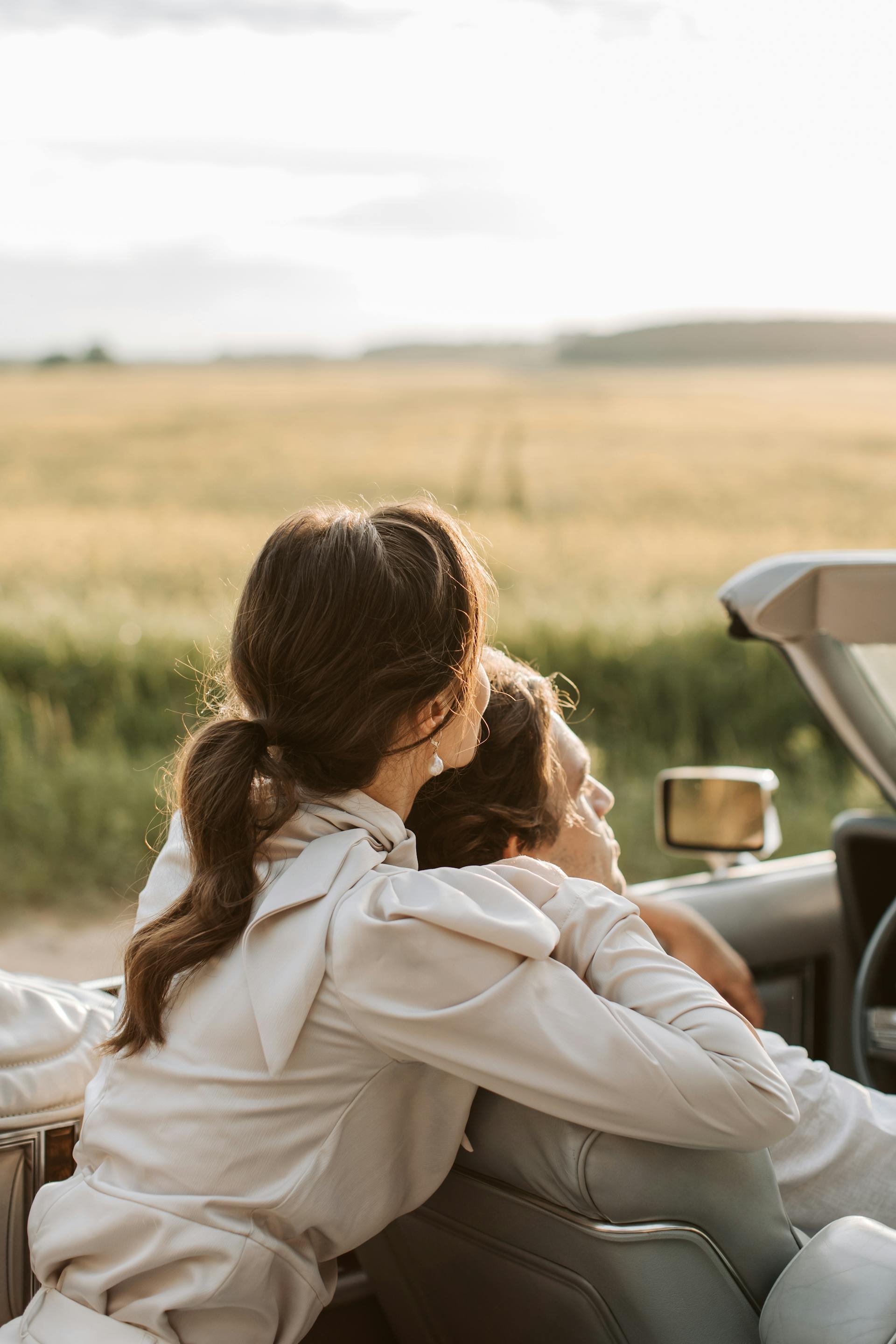 Wedding Website Design, Digital Wedding Stationery, Web Design and Branding for Wedding Professionals | Avelã White. A couple sitting in a convertible car with an open countryside view, woman embracing man, both facing away.