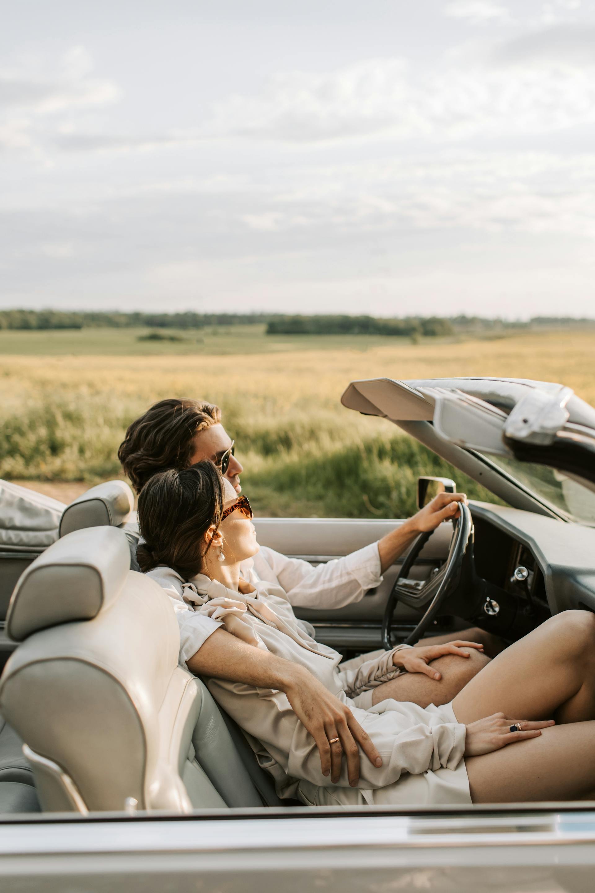 Wedding Website Design, Digital Wedding Stationery, Web Design and Branding for Wedding Professionals | Avelã White. Couple driving in a convertible on a sunny day, relaxing and enjoying the open field view.